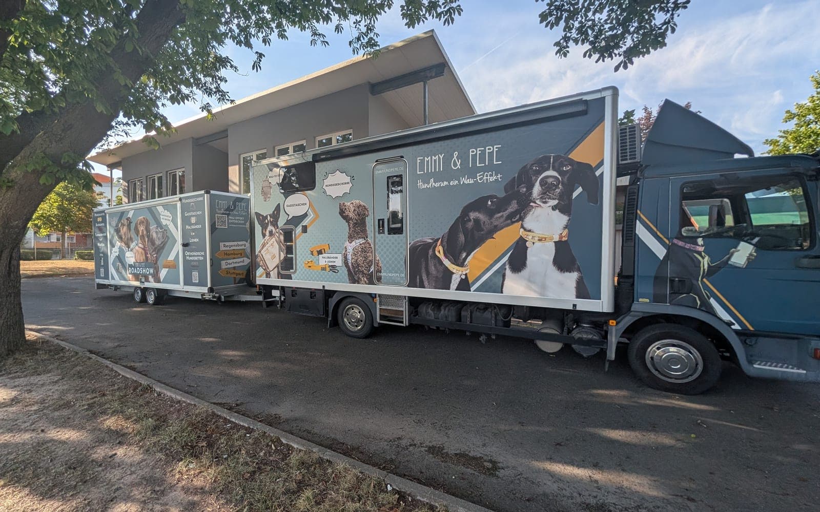 Der EMMY & PEPE Roadshow-LKW mit Anhänger, beklebt mit Hundemotiven und Wegweisern nach Regensburg, Hamburg, Dortmund und Stuttgart.